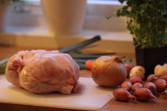 Bilde av hel kylling og grønnsaker på kjøkkenbenken, illustrasjon oppskrift coq au vin